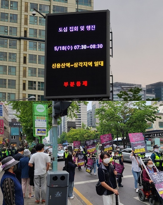 전국장애인차별철페연대가 18일 오전 아모레퍼시픽 본사 앞 횡단보도를 15분간 점거해 “추가경정예산에 장애인권리예산을 반영해달라”고 외친 후, 삼각지역까지 행진하고 있다. (위)전장연의 행진으로 차량 부분 통제를 알리는 전광판 모습(아래)버스정류장에서 전장연의 행진을 지켜보는 시민들 모습.ⓒ에이블뉴스
