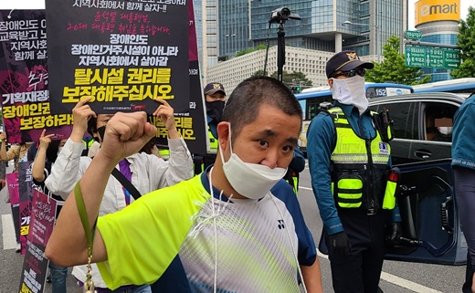 18일 오전 아모레퍼시픽 본사 앞 횡단보도를 점거해 “추가경정예산에 장애인권리예산을 반영해달라”고 외치는 전국장애인차별철폐연대 긴급행동. 투쟁을 외치는 장애인 활동가 뒤로 차량에 타고 있는 시민이 보인다.ⓒ에이블뉴스