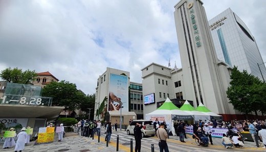 16일 서울시의회 앞 전경. 가운데 도로를 두고 왼쪽에는 탈시설 조례 제정을 반대하는 전국장애인거주시설이용자부모회가 피켓 시위를, 오른쪽에는 탈시설 조례 제정을 촉구하며 천막농성 및 결의대회를 이어가는 전국장애인차별철폐연대 모습.ⓒ에이블뉴스 